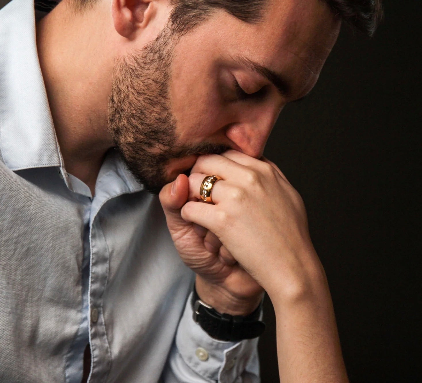 Un homme embrasse tendrement la main de sa partenaire, mettant en valeur une bague d'engagement en or sertie de diamants. Scène d'amour et de fiançailles.